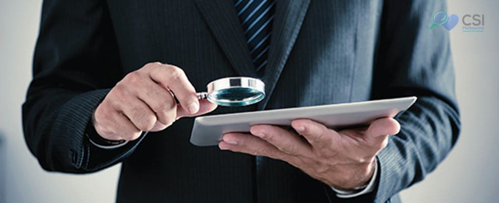 man holding a magnifying glass on his right hand and a tablet on a left hand.